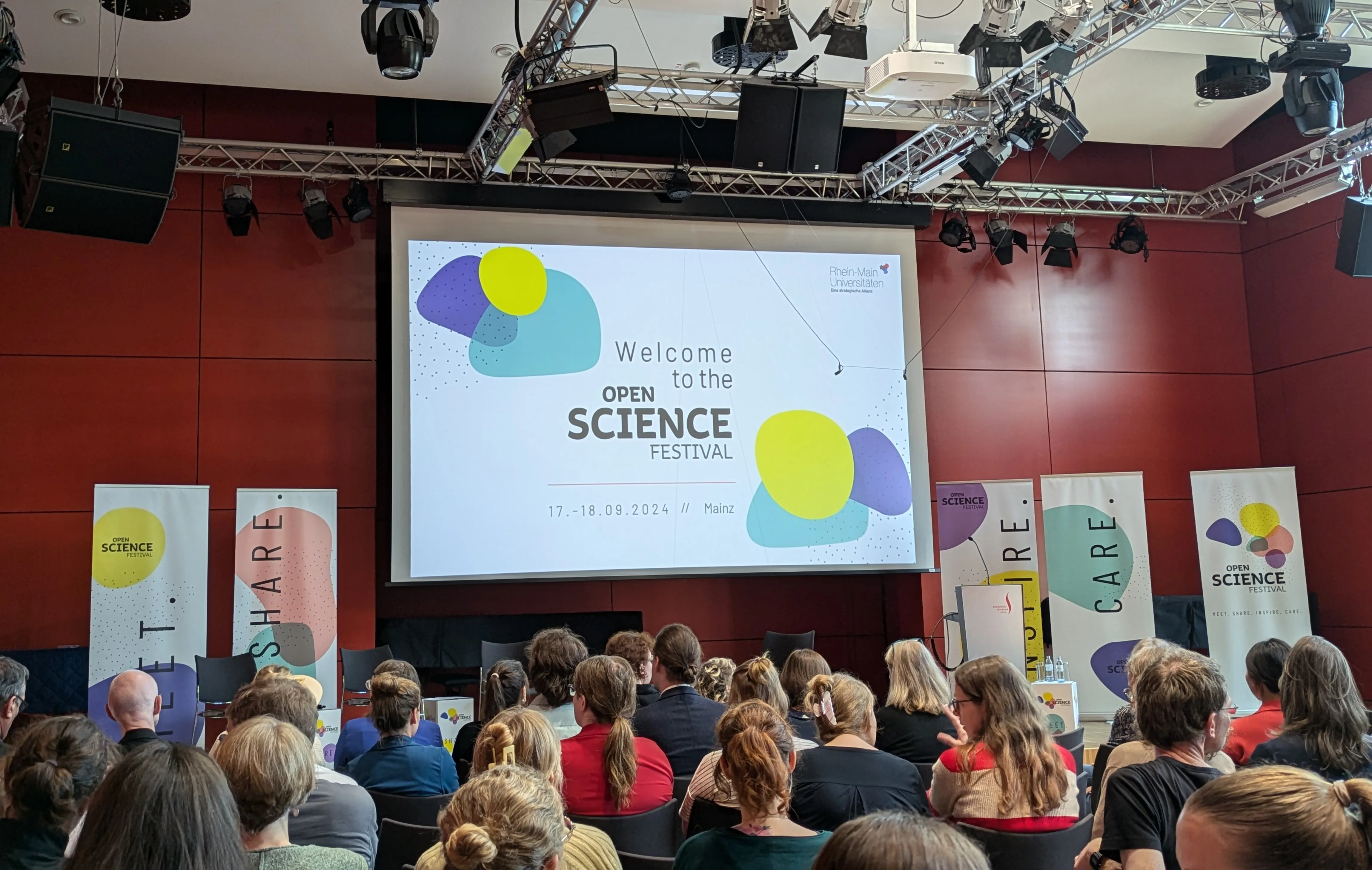 View from the plenum onto the stage. The first slide of the presentation is visible, reading "Welcome to the Open Science Festival".