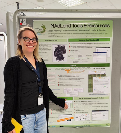Saskia Hiltemann standing in front of the MAdLand poster presented at the MBP2024 conference. Topics covered include Galaxy for user-friendly and FAIR data analysis, the Genome Zoo as a comprehensive protein database for plant and algal genomes. TAPscan as a tool for detecting transcription associate proteins. DataPLANT ARCs for FAIR and open research data. 